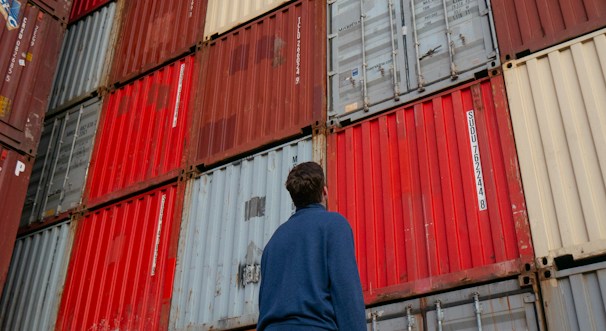 man in blue long sleeve shirt standing in front of red and blue intermodal containers