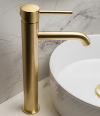 a bathroom sink with a gold faucet next to a white bowl
